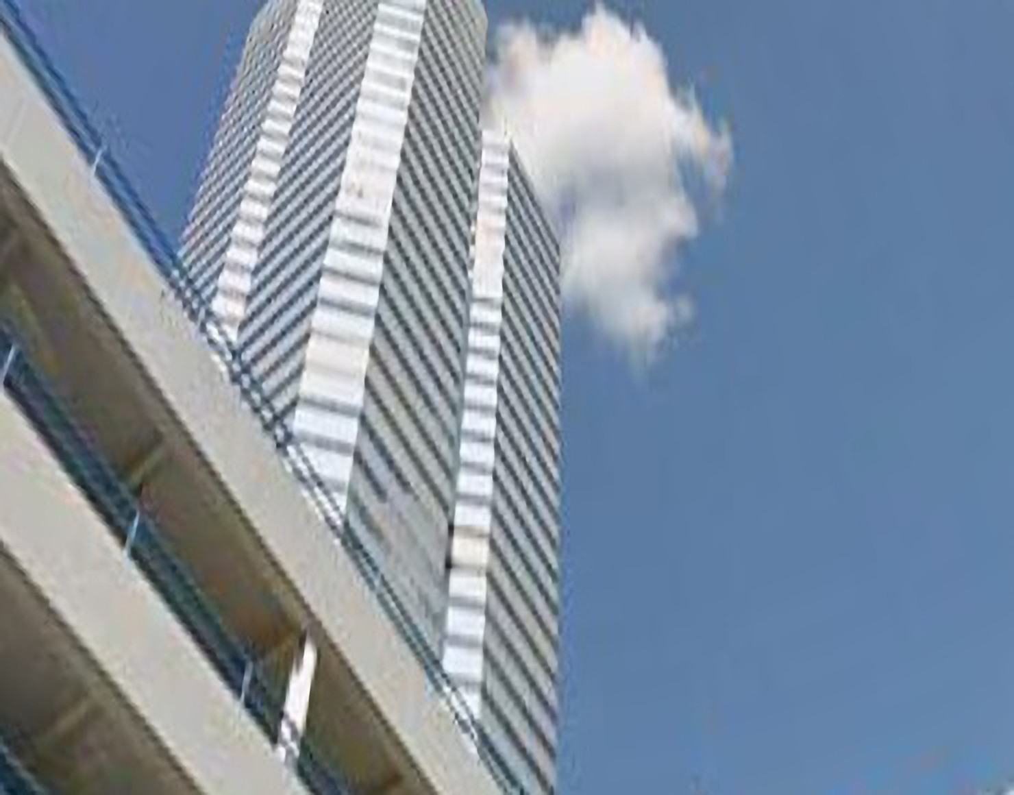An abstract photograph of a modern office building and car park, looking up. Behind it is a cloud and a blue sky.